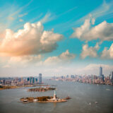 An aerial view of the New York City skyline, with the Statue of Liberty and One World Trade visible