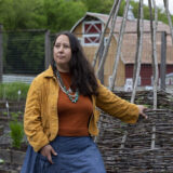 A person in a yellow jacket leans against a wooden farm structure