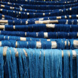 Various strands of blue-dyed yarn drying on white dowels