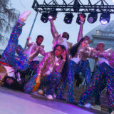 A group of dancers strikes a pose on a brilliantly lit stage