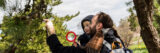 A parent and child use a magnifying glass to examine winter conifers