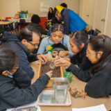 Children and teachers take part in a plant class while examining soil and leaves