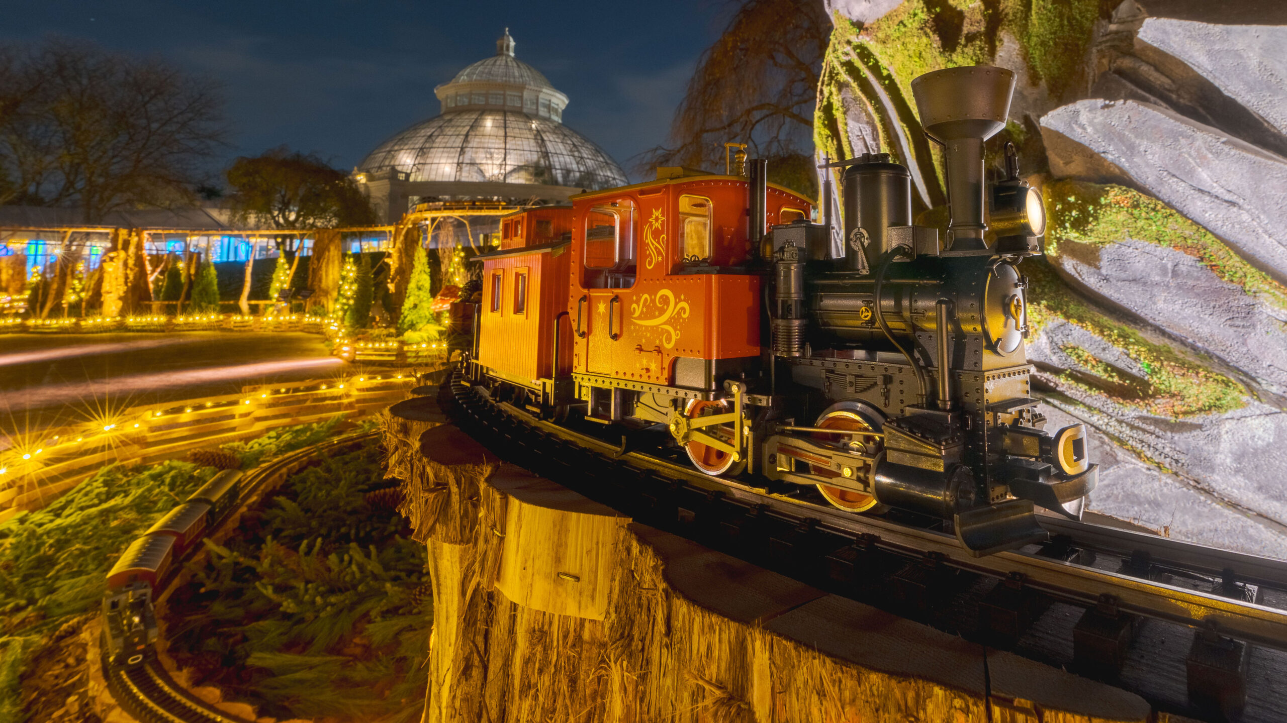 A model train travels through a warmly lit garden holiday display
