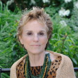 A person in a leopard print shirt and beige sweater poses for a photo in front of a verdant outdoor space