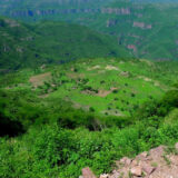 Photo of Wixarika village in Jalisco Mexico; it is a circular green plateau in the middle surrounded by lush, green, mountainous