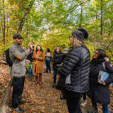 A group of people explore a trail in a colorful fall forest