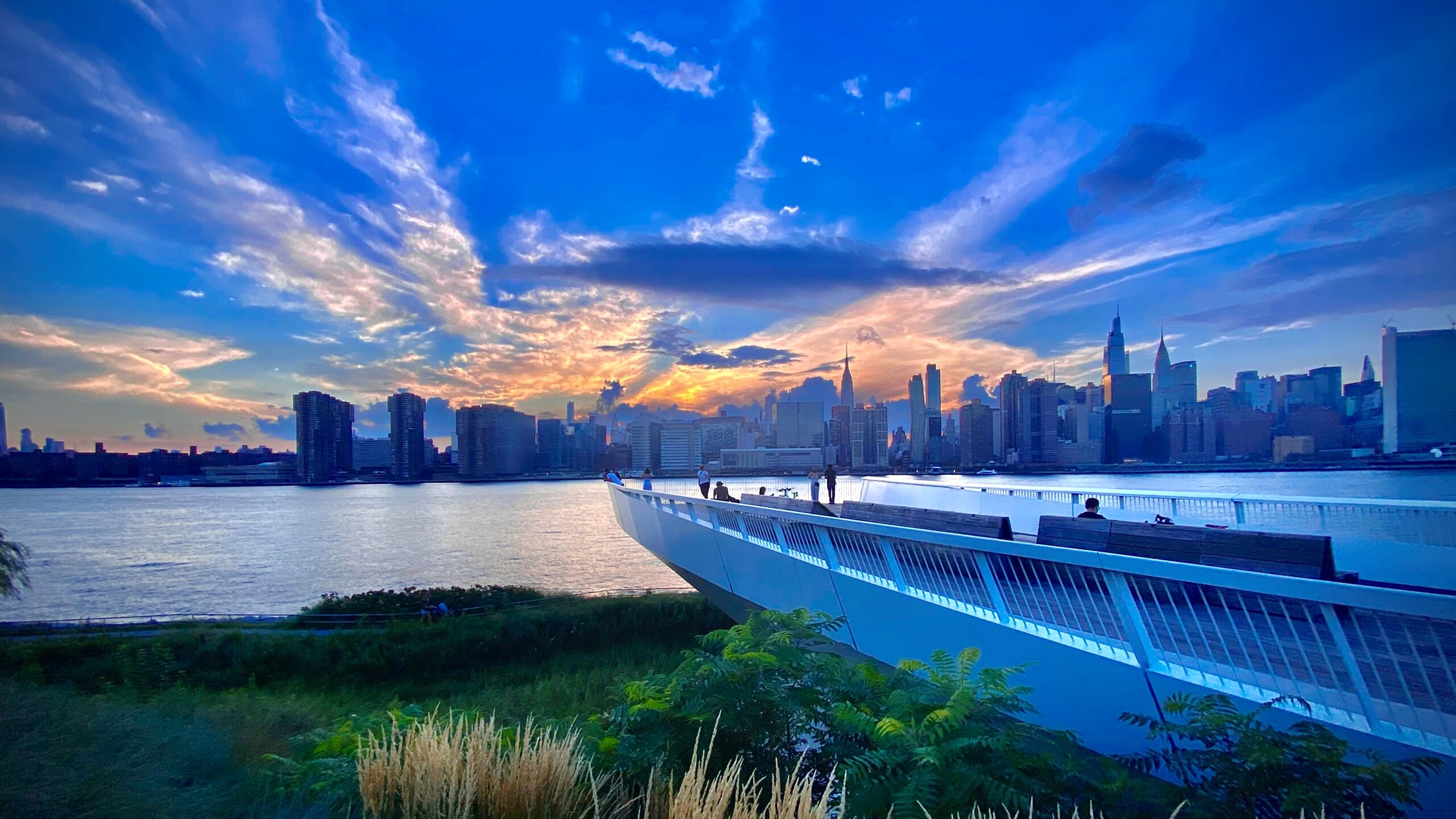 A vivid blue scene of a city skyline viewed from an overlook along a waterfront