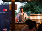 a person with a white button down and grey apron on leads a cooking demonstratio