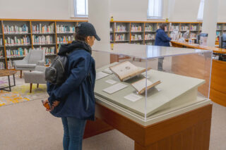 A person with a hat looking in a display case where books are displayed.