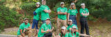 A group of people in bright green shirts poses for a photo in a forested outdoor space