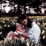 A parent and child sit among a field of white and yellow flowers