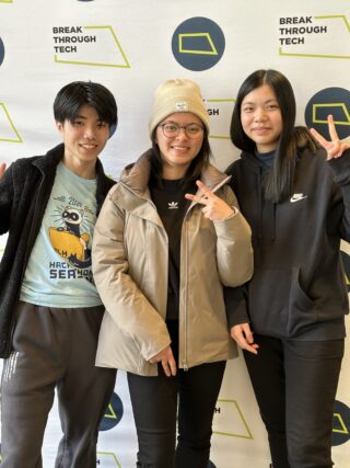 Three people in jackets stand in front of a wall filled with the words "Break Through Tech."