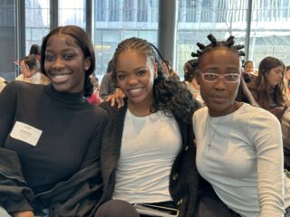 Three young women sitting close to each other smile at the camera.