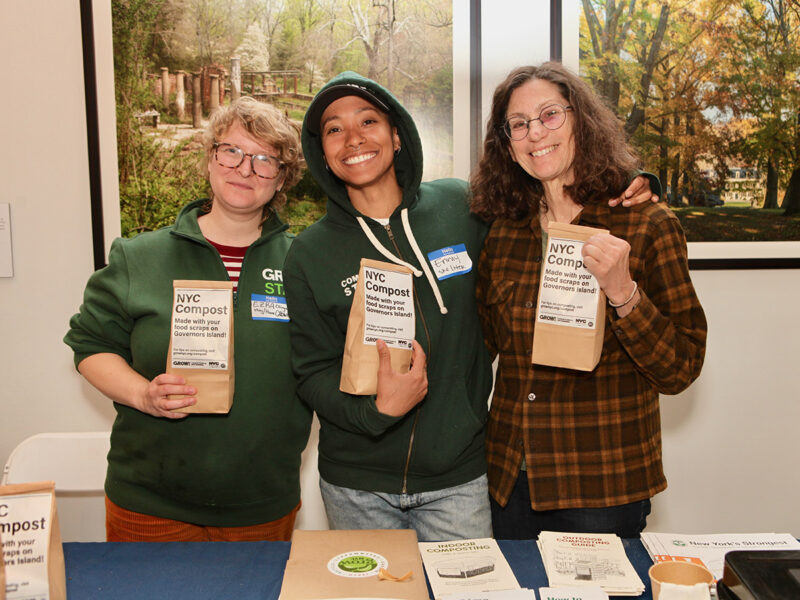 Three people pose for a photo while holding up brown bags of compost