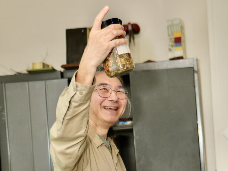 A person in a khaki shirt holds up a jar of compost material