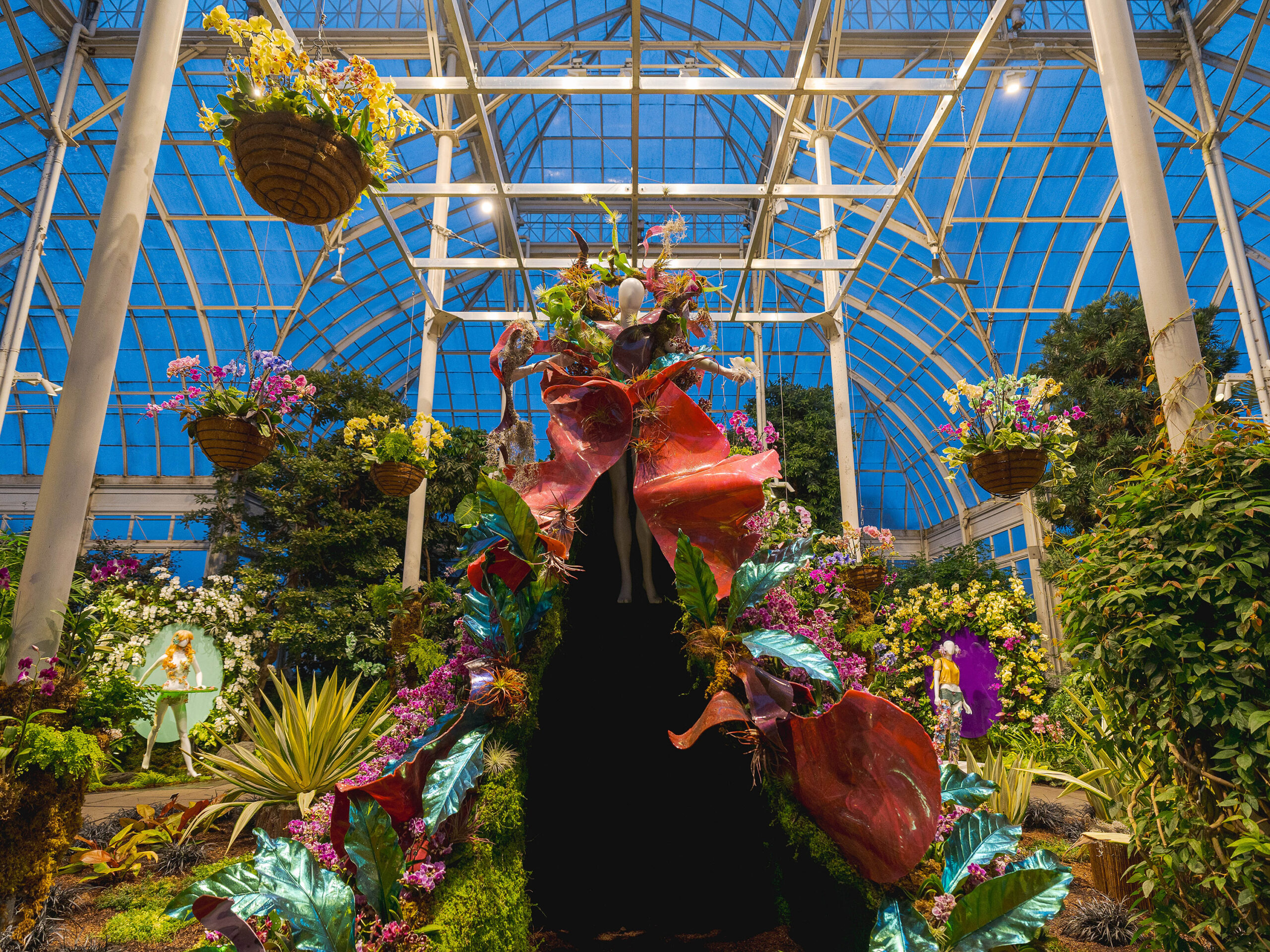 An evening view of an elaborate flower exhibition after dark, featuring mannequins covered in colorful blooms