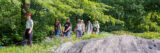 A group of people in summer clothes follow a tour guide through a lush garden setting