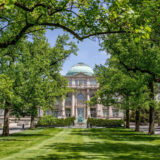 A view of a classical building at the end of a green, tree-lined lawn