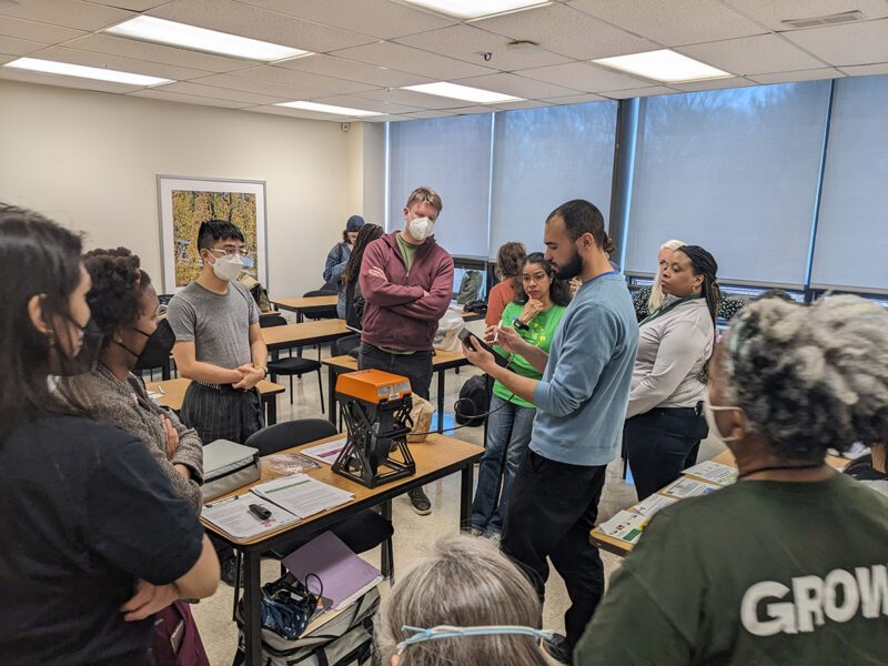 A group of people look on as an instructor demonstrates an object