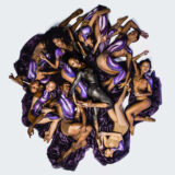 A group of performance artists lies entangled among one another in a circle