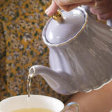 Someone uses a purple teapot to pour a cup of tea