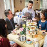 three people are sitting at a table set for tea with lite bites and dessert towers