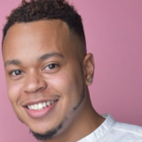 A person with short brown hair poses for a headshot in front of a pink wall