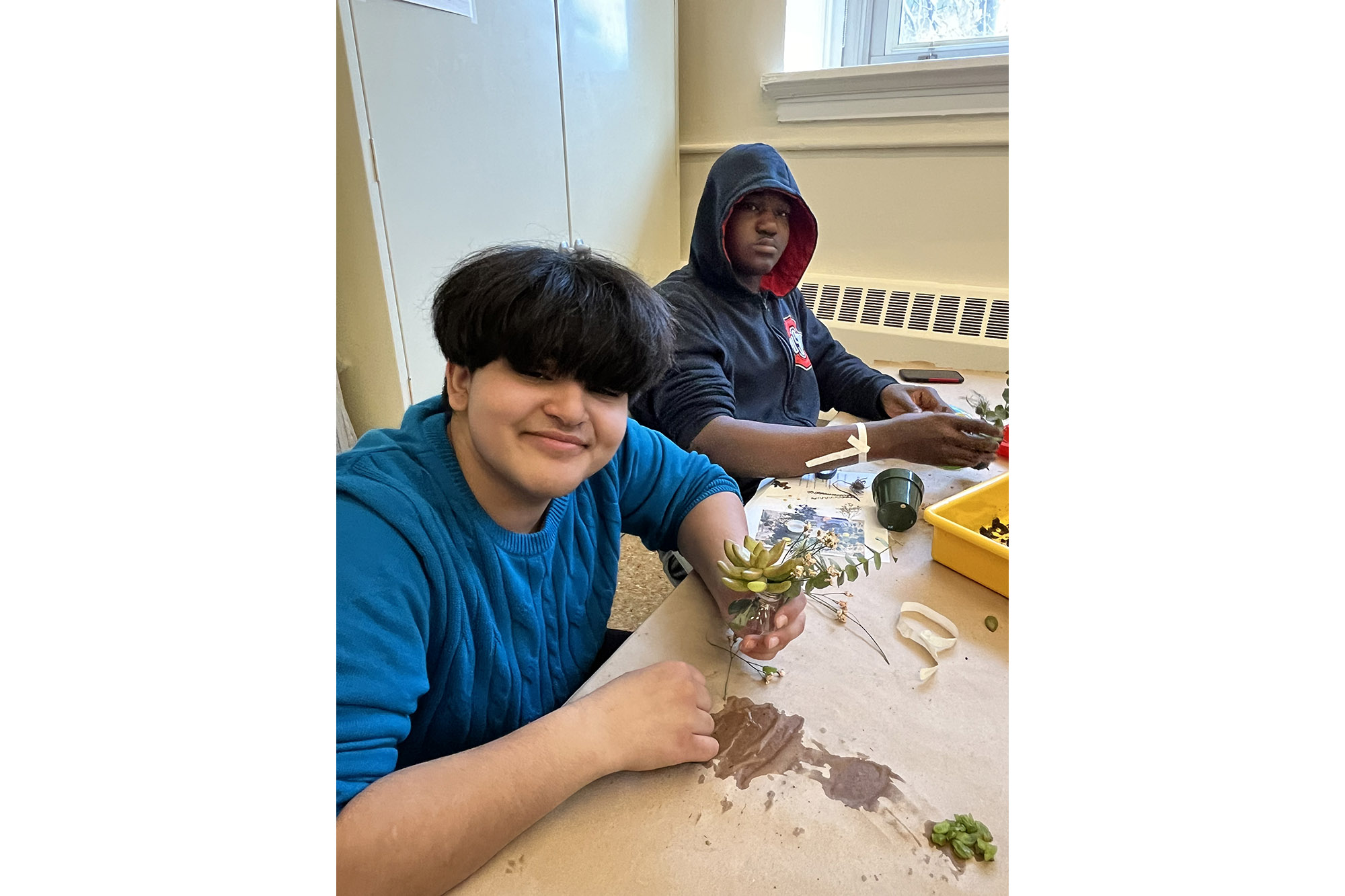 Two students create wearable art with live plants in a classroom setting