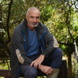 A person in a blue shirt and black sweatshirt poses for a photo outdoors