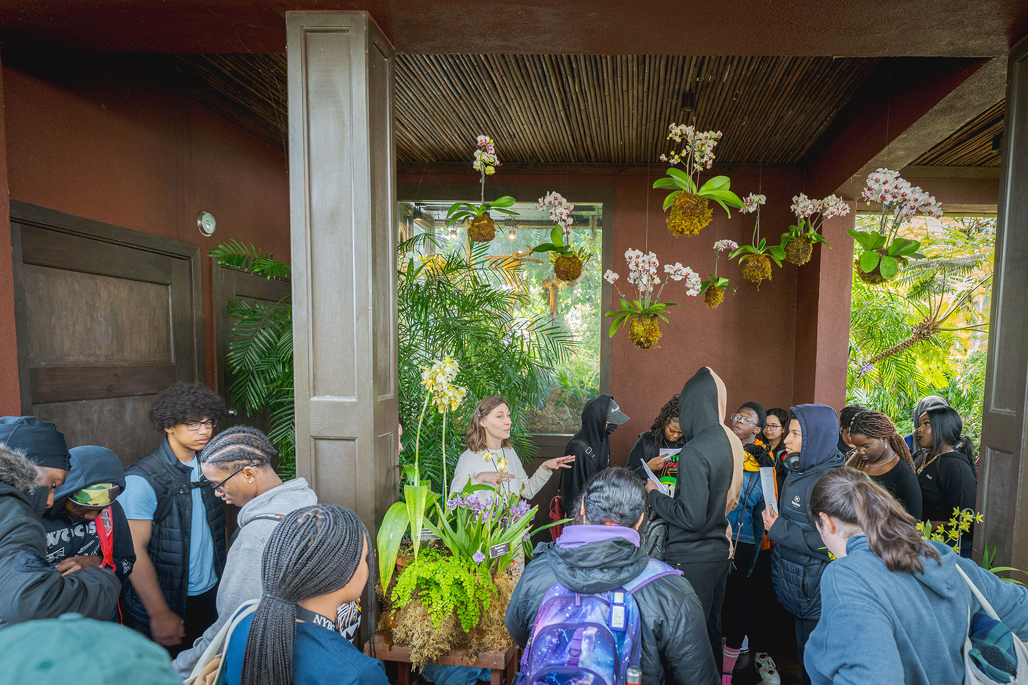 A tour guide speaks with a class of students as they explore a green conservatory