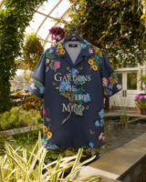 A colorful shirt reading "Gardens of the Mind" hangs on a hanger in a planted conservatory setting