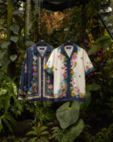 Two colorful shirts hang on clothes hangers in a lush jungle setting