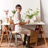 A person works with flower arrangements at a white table