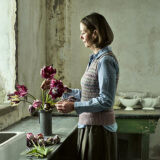 A person creates a vase full of arranged purple tulips