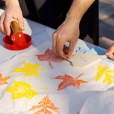 People create orange and yellow stamps of leaf shapes on white paper