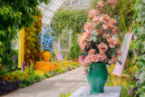 A conservatory full of green plants accompanied by large vases full of colorful flower sculptures