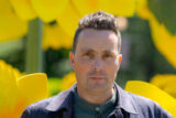 A person in a purple jacket poses for a photo in front of enormous yellow flower sculptures