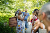 A person wearing a basket on their back demonstrates foraging techniques to a tour group