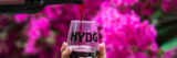 A person pours red wine into a glass tumbler labeled "NYBG"