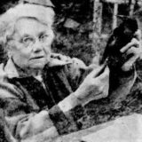 A black and white photo of a person in a flannel jacket putting a band on the leg of a captured bird