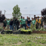 A group of people in gardening clothes pose for a photo in an outdoor garden
