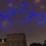 Blue and yellow lights form swirls and stars in the night sky above a large building