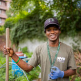 A person holding a shovel poses for a photo in an outdoor garden