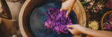 hands of artisan dyeing fabric using natural plant based dyes in wooden tub