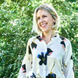 A person in a white floral shirt poses outdoors for a photo
