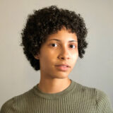A person with short black hair and a green shirt poses for a photo
