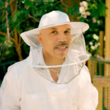 A person in a beekeeping outfit poses for a photo outdoors