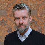 A person with short gray hair and a beard poses for a photo