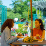 Two people sit at a cafe outdoors, enjoying drinks and conversation