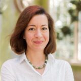 Person with red-brown hair wearing necklace and white shirt looking ahead
